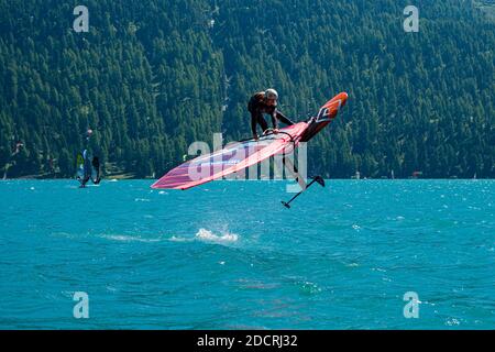 Un windsurf con vela rossa salta sul lago Silvaplana. Foto Stock