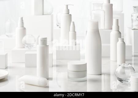 Bottiglie e vasetti bianchi con vari prodotti di bellezza posti vicino cubetti su tavolo in marmo bianco Foto Stock