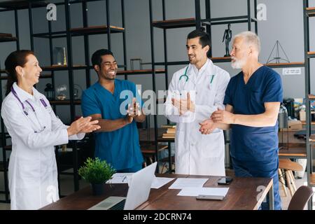 Successo felice grigio-capelli maturo capo medico capo squadra Get applausi in una sala d'ufficio leggera Foto Stock