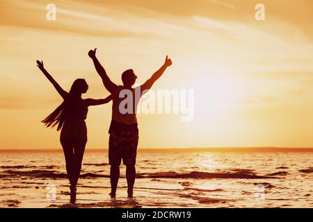 Happy Couple si erge con le braccia sollevate alla spiaggia del tramonto Foto Stock