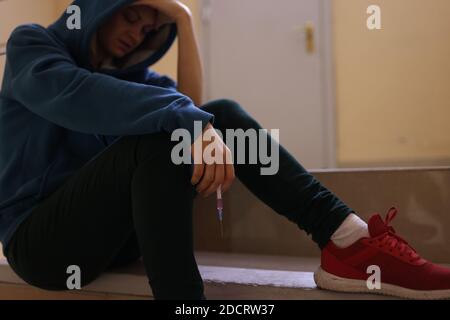 Addict si siede con la testa in giù e tiene la siringa nelle mani. Foto Stock