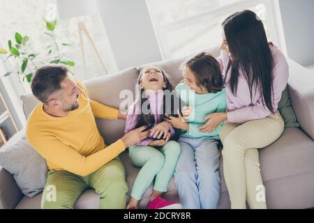 Foto della grande famiglia quattro membri siedono daddy divano solletico figlia indossare colorati pantaloni maglione in soggiorno interno Foto Stock