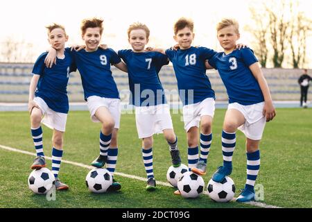 Ragazzi della scuola sportiva in squadra di calcio. Gruppo di bambini in maglia da calcio Sportswear in piedi con palle sul campo da erba. Happy Smiling Kids in Sport Tea Foto Stock