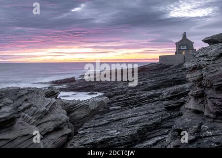 Alba in Northumberland a Howick. Le onde si infrangono sulla costa rocciosa mentre il Sole sorge sul Mare del Nord. Foto Stock
