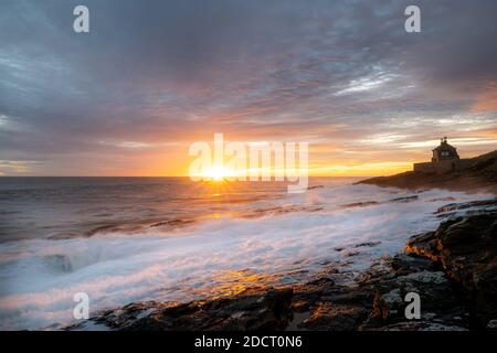 Alba in Northumberland a Howick. Le onde si infrangono sulla costa rocciosa mentre il Sole sorge sul Mare del Nord. Foto Stock