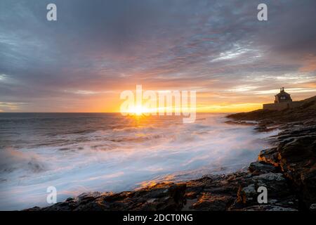 Alba in Northumberland a Howick. Le onde si infrangono sulla costa rocciosa mentre il Sole sorge sul Mare del Nord. Foto Stock