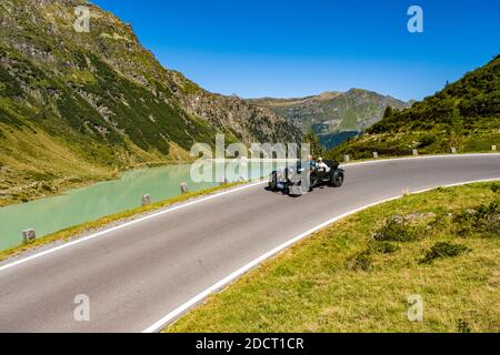 Un'auto d'epoca Bentley 4,5 L le Mans Open Tourer che passa accanto a un lago sulla Silvretta Hochalpenstrasse durante il Rally di Arlberg Classic Car. Foto Stock