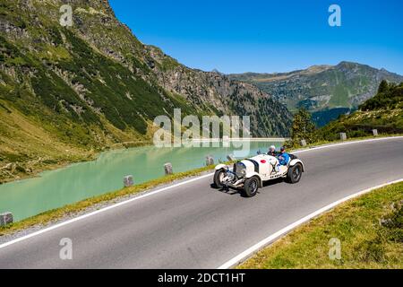 Un'auto d'epoca Mercedes-Benz SSKL che oltrepassa un lago sulla Silvretta Hochalpenstrasse durante il raduno di auto d'epoca Arlberg. Foto Stock
