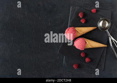 Gelato al lampone in coni di cialde con vista dall'alto del tavolo nero. Estate rinfrescante sorbetto. Foto Stock