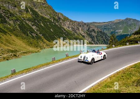 Un'auto d'epoca Jaguar XK 120 OTS se Roadster che passa accanto a un lago sulla Silvretta Hochalpenstrasse durante il raduno di auto classiche Arlberg. Foto Stock