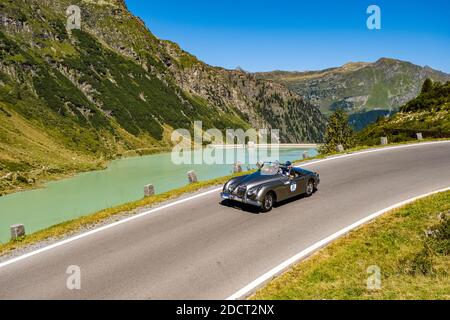 Un'auto d'epoca Jaguar XK 150 Cabrio che passa accanto a un lago sulla Silvretta Hochalpenstrasse durante il raduno di auto d'epoca Arlberg. Foto Stock