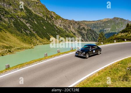 Un'auto d'epoca Lancia Aprilia Berlina che oltrepassa un lago sulla Silvretta Hochalpenstrasse durante il raduno di auto d'epoca Arlberg. Foto Stock