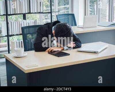Giovane uomo d'affari asiatico con problemi, stanco, stressato e triste noioso seduta con testa giù sulla sua scrivania in ufficio. Frustrato lavoratore mentale h Foto Stock