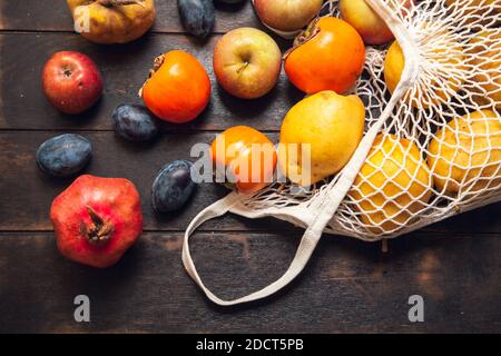 Vari frutti autunnali in una borsa a rete su uno sfondo di legno scuro. Foto Stock