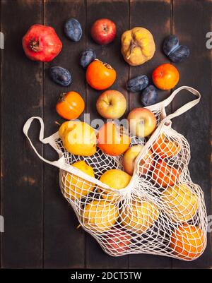 Vari frutti autunnali in una borsa a rete su uno sfondo di legno scuro. Foto Stock