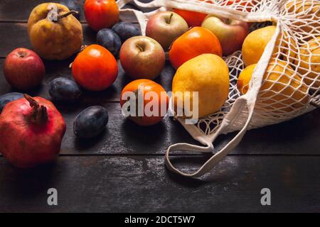 Vari frutti autunnali in una borsa a rete su uno sfondo di legno scuro. Foto Stock