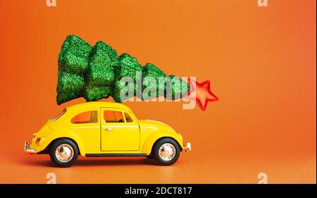 Odessa Ucraina 06 12 2019: Auto giocattolo retrò giallo che porta l'albero di natale festivo sul tetto. Albero di Capodanno sul tetto dell'auto. Sfondo di colore arancione con Foto Stock