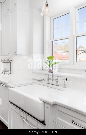 Un lussuoso lavello da cucina. Il lavello è dotato di un rubinetto cromato su un lavello di grembiule bianco davanti alle finestre. Foto Stock