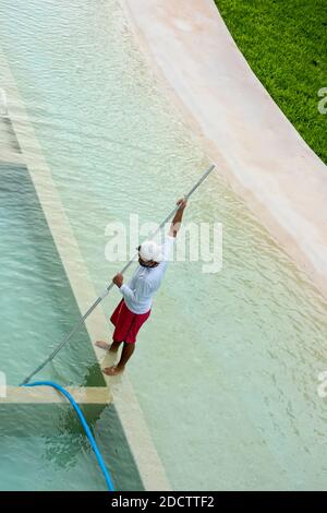Uomo giovane sconosciuto pulisce la piscina, Playa del Carmen, Messico. Orientamento verticale dello schermo Foto Stock