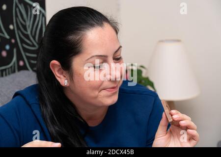 Donna adulta modello sul divano mangiare dolce gustoso cioccolato bar come un dessert casalingo che fa un'espressione sorridente Foto Stock