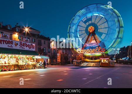 Giostra illuminata e stalla mobile con dolci sulla piazza della città in serata come parte delle tradizionali celebrazioni natalizie ad Alba, Italia. Foto Stock