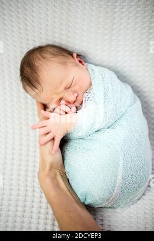 Cute bambino neonato addormentato avvolto in blu posa su la mano della madre Foto Stock