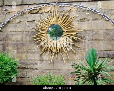 Specchio rotondo con un decor di rami disposti in una cerchio nella forma del sole appende su un muro di pietra all'aperto Foto Stock