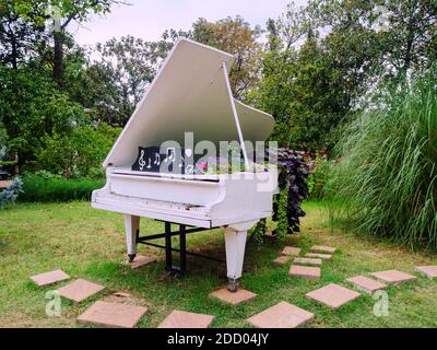 Grande pianoforte bianco decorativo decorato con fiori in piedi parco tra piante verdi alberi abd Foto Stock