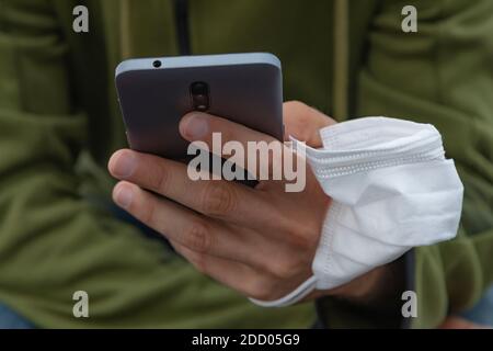 Un giovane, afferrando una maschera protettiva, tiene un telefono cellulare intelligente con la mano, la Spagna. Foto Stock