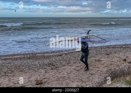 Il surfista anziano in costume da bagno nero cammina sulla riva e trasporta le sue attrezzature sulla testa, Smidstrup, Danimarca, 22 novembre 2020 Foto Stock