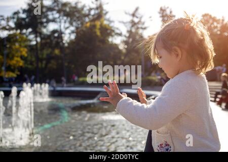 adorabile bambina guarda le fontane nel parco in una giornata di sole. Foto Stock