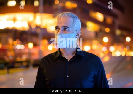 Uomo di notte per strada con maschera facciale protettiva per proteggere dal virus covid 19 corona mentre si pensa Foto Stock