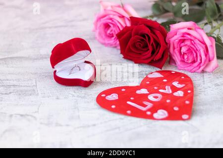 Anello di nozze all'interno della scatola di velluto rosso per l'anello di impegno accanto alla carta di San Valentino e bouquet di rose con spazio per il testo. Regalo romantico per San Valentino Foto Stock