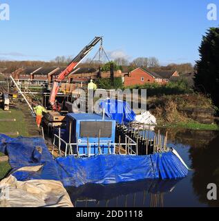 Una nuova traversa di blocco in legno viene sollevata da una barca da lavoro ed è posizionata sull'atterraggio di blocco come parte del montaggio di nuovi cancelli della testa a Ell Meadow Lock vicino a Wigan. Foto Stock