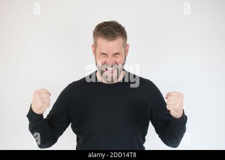 Felice vincitore. Felice giovane bell'uomo che gesticola e tiene la bocca aperta mentre si alza su sfondo bianco Foto Stock