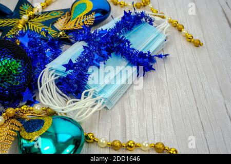 Composizione con maschera medica blu corona virus e decorazione invernale con palline d'oro su sfondo di legno offuscato. Buon Natale in covid-19 pa Foto Stock