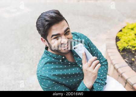 Un primo piano con vista dall'alto di un uomo ispanico che si erge all'esterno e sorridendo con il telefono tra le mani Foto Stock