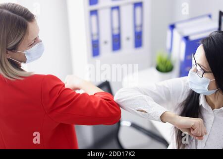 Due uomini d'affari in maschere di protezione che toccano i gomiti in ufficio Foto Stock