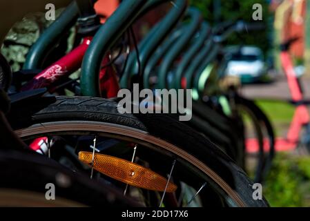 Biciclette parcheggiate di fila, in ambiente urbano in una giornata di sole. Mettere a fuoco su una ruota di una bicicletta. Foto Stock