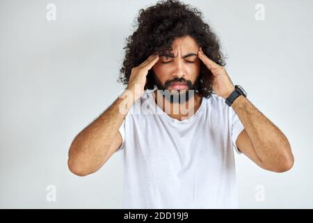 giovane indiano arabo con capelli lunghi ha mal di testa, soffre di emicrania, ha un attacco di emicrania. isolato sfondo bianco Foto Stock