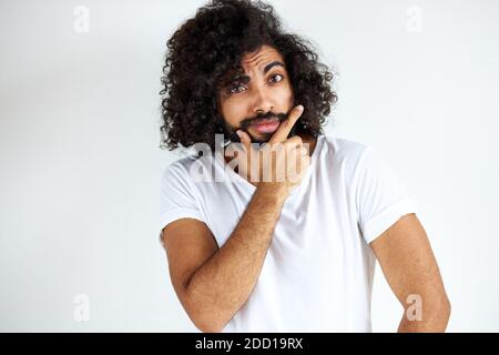 il maschio arabico determinato con la barba sta pensando e guardando preoccupato, in piedi contro sfondo bianco. Foto Stock