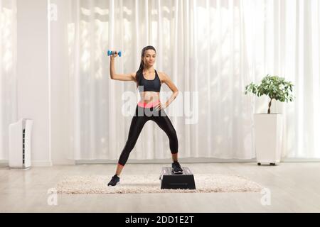 Ritratto a lunghezza intera di una giovane donna che esercita il passo aerobico con un manubri a casa Foto Stock