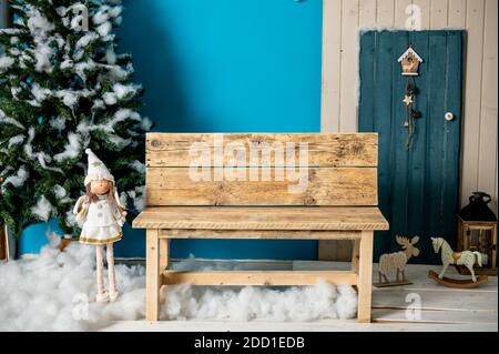 Studio decorativo di Natale con una casa con porta blu, panca in legno e sci, pupazzo di neve, nubi finte e neve Foto Stock