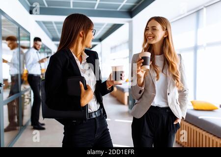 I colleghi di affari felici stanno discutendo qualcosa e bevendo il caffè mentre camminando lungo il corridoio dell'ufficio durante Foto Stock