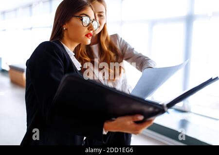 I giovani colleghi di lavoro sono felici di comunicare mentre camminano lungo il corridoio in ufficio con una cartella con documenti Foto Stock