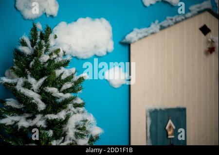 Studio decorativo di Natale con una casa con porta blu, panca in legno e sci, pupazzo di neve, nubi finte e neve Foto Stock