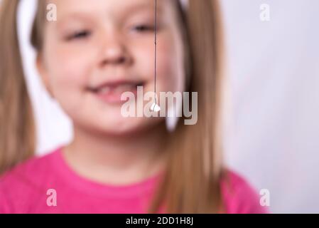 La bambina in rosa tiene un dente tirato fuori del latte su una filettatura Foto Stock