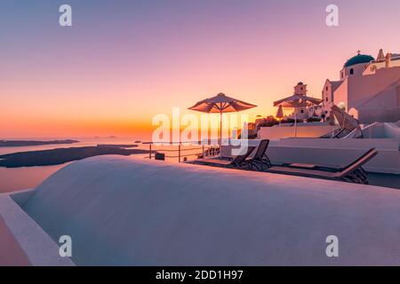 Terrazza al tramonto sull'isola di Santorini, Grecia. Splendido resort con vista sulla caldera e tramonto. Relax vibrazioni, ombrellone e sedie, tavolo. Vacanze estive Foto Stock