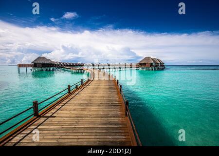 Maldive villa su pali d'acqua, viaggi estivi di lusso. Mattina luce del sole, lungo molo di legno sotto il cielo blu nuvoloso. Bungalow di lusso, mare incredibile Foto Stock