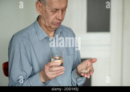 Il vecchio tiene le pillole e un bicchiere d'acqua nelle sue mani. Problemi di salute negli anziani, il processo di invecchiamento. Foto Stock
